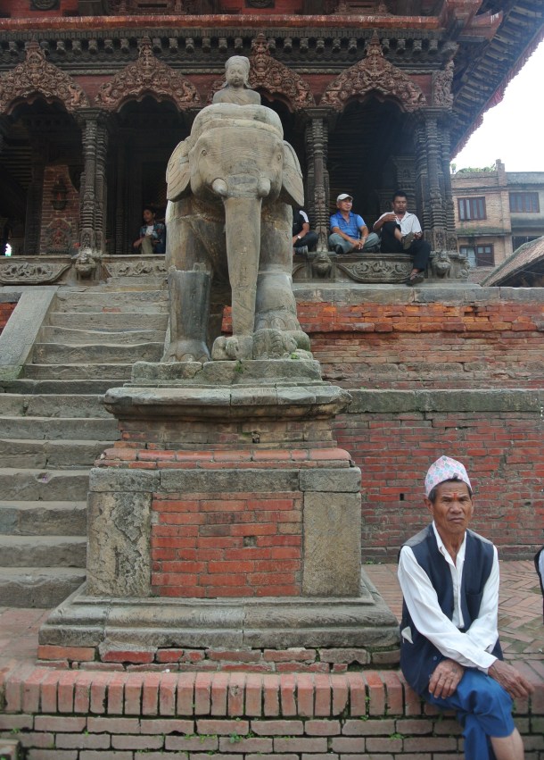 a Nepali man sitting by an elephant statue in Bhanktapur's Durbar Square